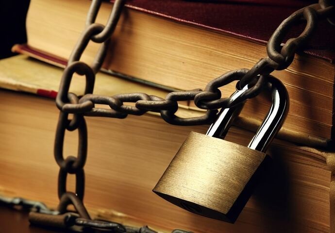 A stack of books wrapped in heavy chains secured with a brass padlock, symbolizing censorship or restricted access to knowledge.