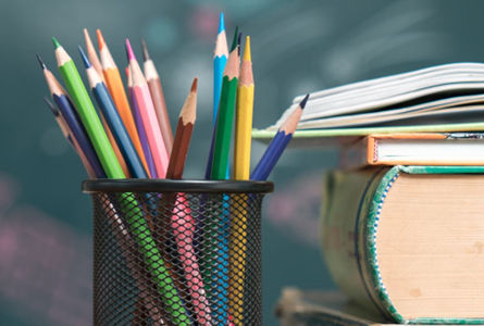 Pencils in a container standing up and a stack of textbooks and a notebook on top